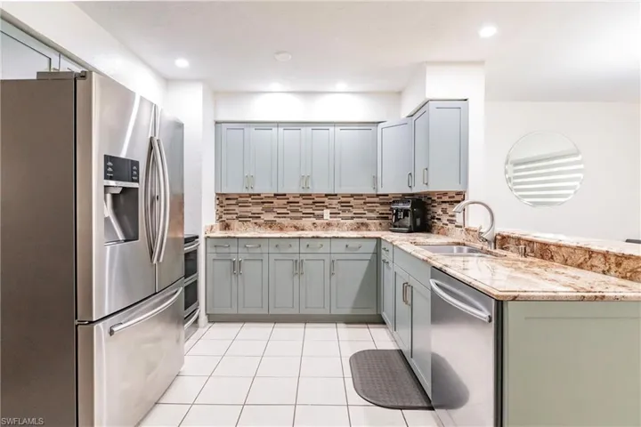 Kitchen with light tile patterned flooring, sink, appliances with stainless steel finishes, light stone countertops, and decorative backsplash