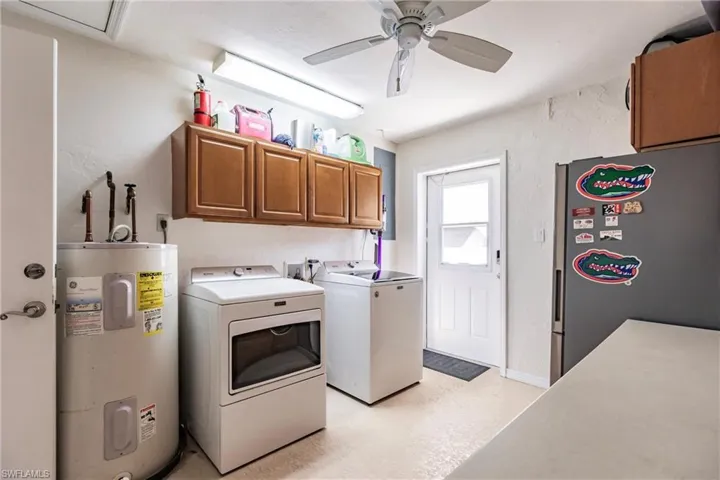 Laundry room featuring ceiling fan, electric water heater, cabinets, and washer and dryer