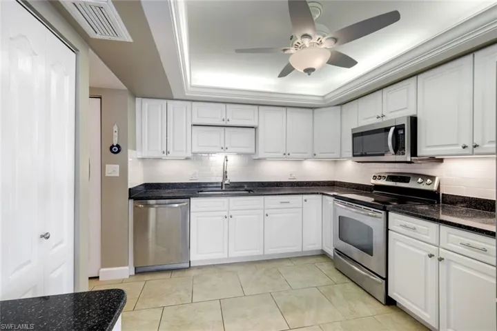 Kitchen featuring appliances with stainless steel finishes, a raised ceiling, white cabinets, and crown molding