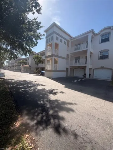 Multi-story building featuring stucco exterior with contrasting trim bands, multiple private balconies with white railings, arched garage doors, and visible palm trees