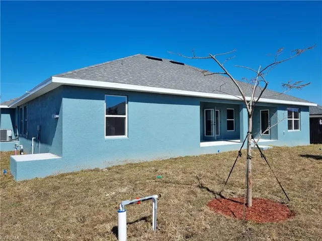 Rear view of house featuring stucco siding, a lawn, a patio area, and roof with shingles