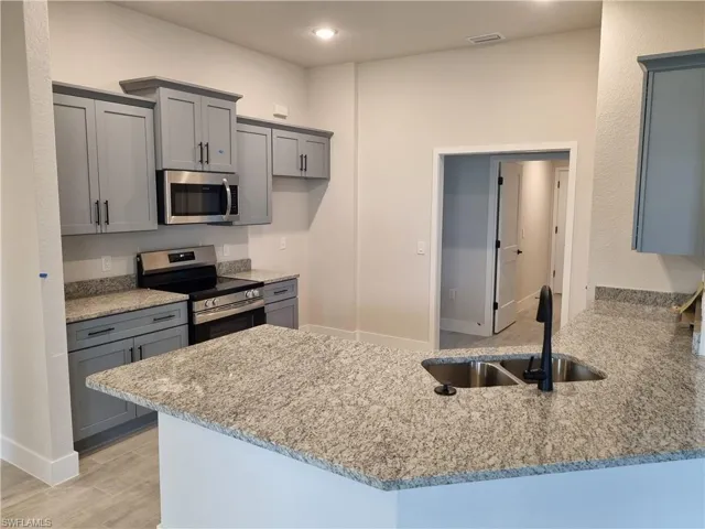 Kitchen featuring gray cabinets, stainless steel appliances, a peninsula, light stone countertops, and light wood finished floors