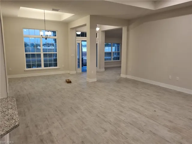 Unfurnished living room featuring a raised ceiling, a chandelier, and light wood-style floors