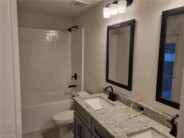 Bathroom with a textured wall, double vanity, and bathing tub / shower combination