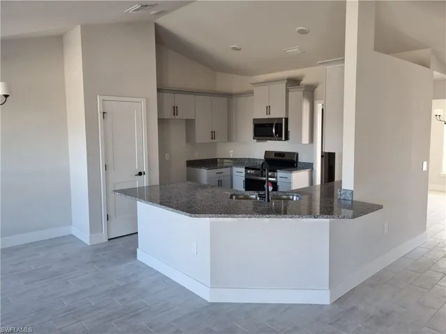 Kitchen with dark stone counters, stainless steel appliances, a peninsula, wood tiled floors, and vaulted ceiling