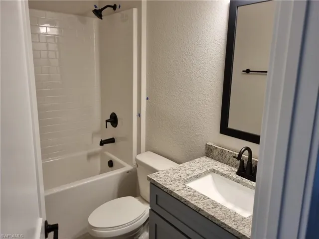 Full bathroom featuring a textured wall, vanity, and bathtub / shower combination