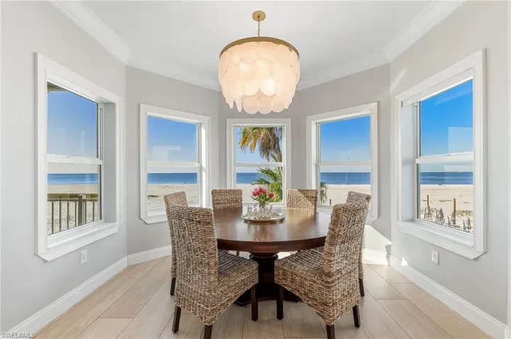Dining room with ornamental molding, view of water and beach, light wood-style floors, and a chandelier