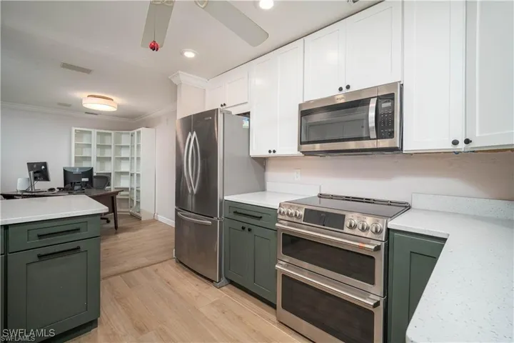 Kitchen featuring stainless steel appliances, dual-tone cabinetry, light-toned countertops, and wood-finish flooring