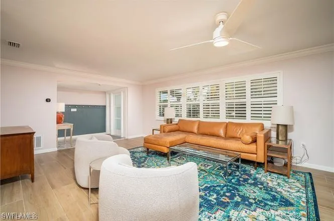Spacious living area featuring wood-finish flooring, crown molding, and a ceiling fan with integrated lighting