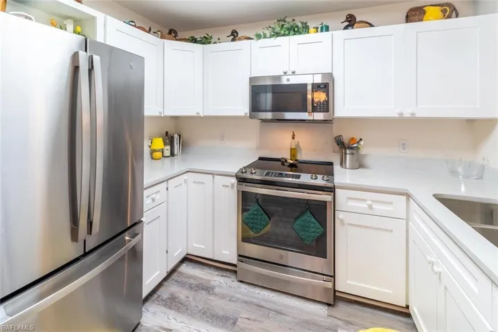 Kitchen with appliances with stainless steel finishes, white cabinets, light wood-type flooring, and light stone countertops