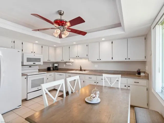 Kitchen featuring a raised ceiling, white appliances, sink, white cabinetry, and ceiling fan