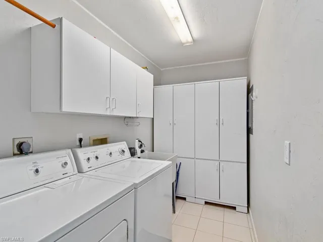 Washroom with light tile patterned floors, sink, cabinets, and washing machine and dryer