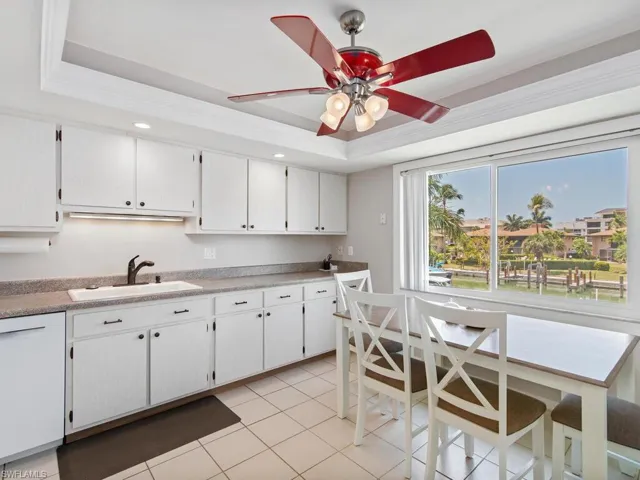 Kitchen with light tile patterned floors, dishwasher, ceiling fan, a raised ceiling, and white cabinets