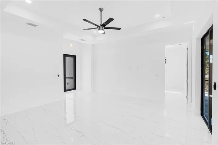 Empty room with a tray ceiling, a ceiling fan, recessed lighting, and light marble finish flooring