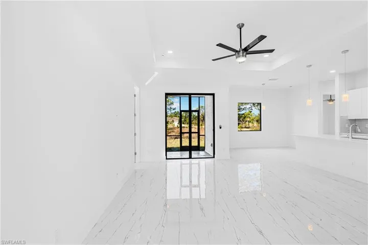 Unfurnished living room featuring a tray ceiling, light marble finish flooring, recessed lighting, and ceiling fan