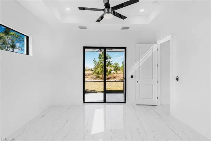 Empty room with a ceiling fan, a raised ceiling, light marble finish floors, and recessed lighting