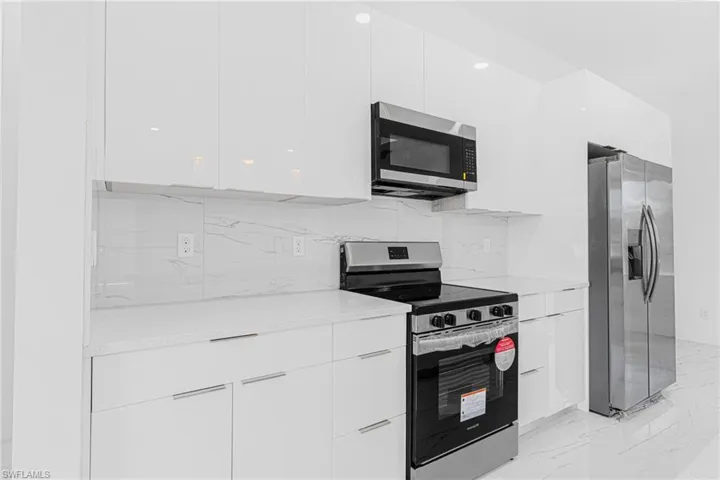 Kitchen featuring modern cabinets, appliances with stainless steel finishes, tasteful backsplash, light marble finish floors, and light countertops
