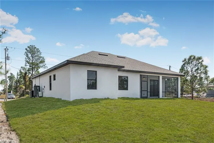 Rear view of house featuring stucco siding, a lawn, a shingled roof, and a sunroom