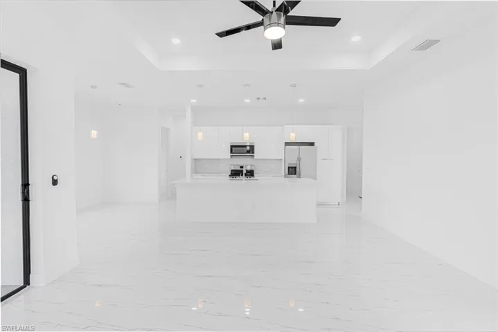 Unfurnished living room with a tray ceiling, light marble finish flooring, ceiling fan, and recessed lighting