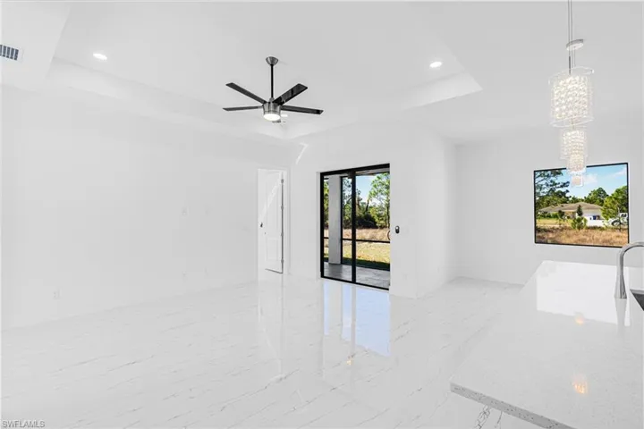 Empty room featuring a raised ceiling, light marble finish flooring, recessed lighting, a chandelier, and ceiling fan
