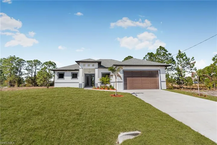 Prairie-style home with stucco siding, concrete driveway, a garage, and a front lawn