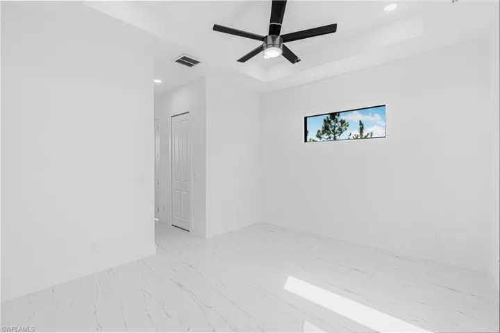 Empty room featuring recessed lighting, ceiling fan, light marble finish flooring, and a tray ceiling