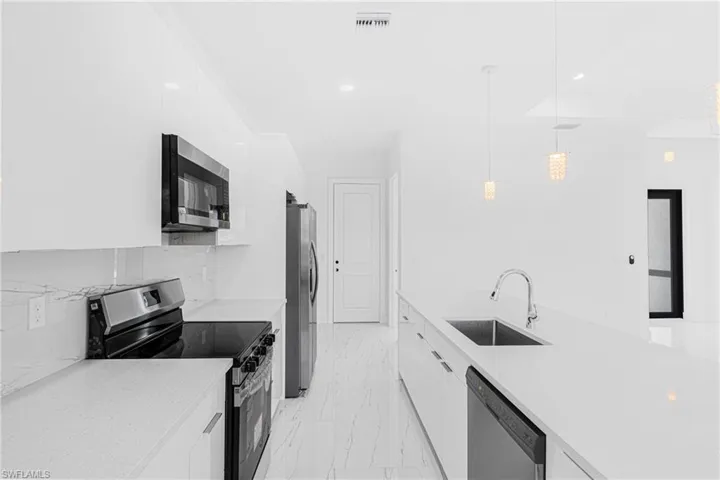 Kitchen with modern cabinets, appliances with stainless steel finishes, white cabinetry, recessed lighting, and light marble finish floors