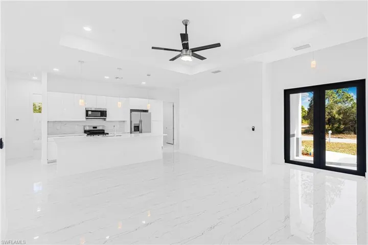 Unfurnished living room featuring a tray ceiling, a ceiling fan, french doors, recessed lighting, and light marble finish flooring