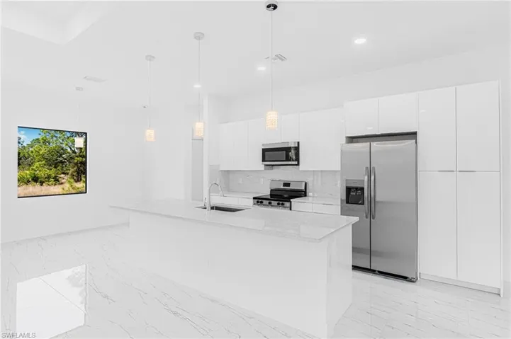 Kitchen featuring light marble finish flooring, appliances with stainless steel finishes, white cabinets, a center island with sink, and recessed lighting