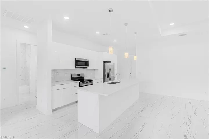 Kitchen featuring modern cabinets, white cabinets, light marble finish flooring, stainless steel appliances, and recessed lighting