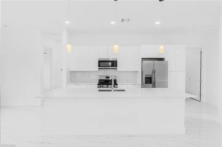 Kitchen with appliances with stainless steel finishes, light marble finish floors, white cabinets, light countertops, and a kitchen island with sink