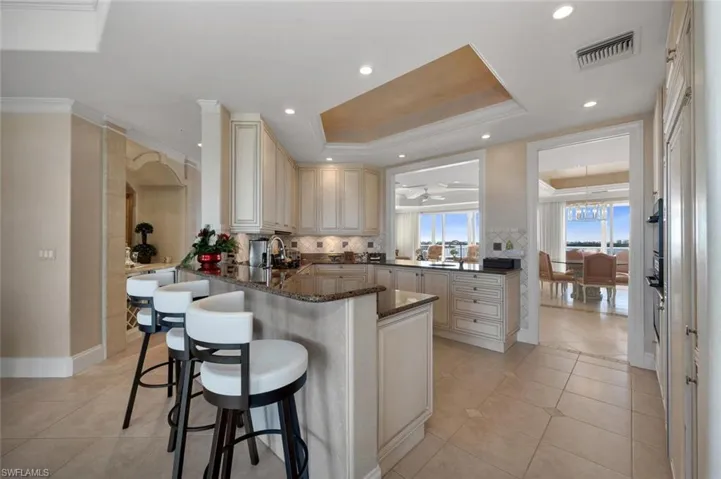 Kitchen with kitchen peninsula, a kitchen bar, dark stone counters, a tray ceiling, and light tile patterned floors