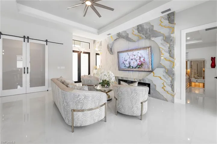 Living space featuring a dramatic accent wall with integrated fireplace, tray ceiling, and polished tile flooring