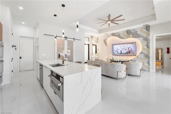 Open-concept living area featuring a large kitchen island with a built-in microwave, white tile flooring, and a decorative wall panel with integrated lighting