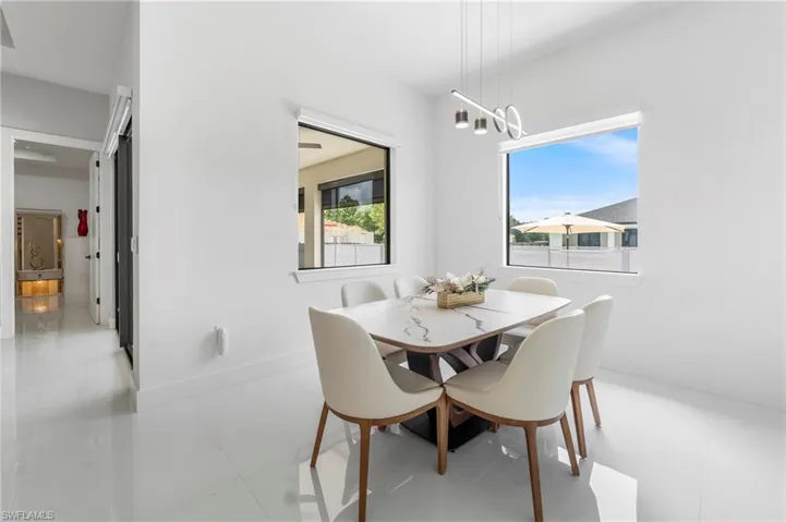 Spacious dining area featuring a modern linear chandelier, white walls, and large windows