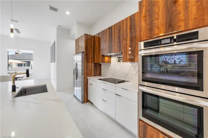 Modern kitchen featuring light wood-grain cabinetry, integrated stainless steel appliances, and a white countertop with a waterfall edge