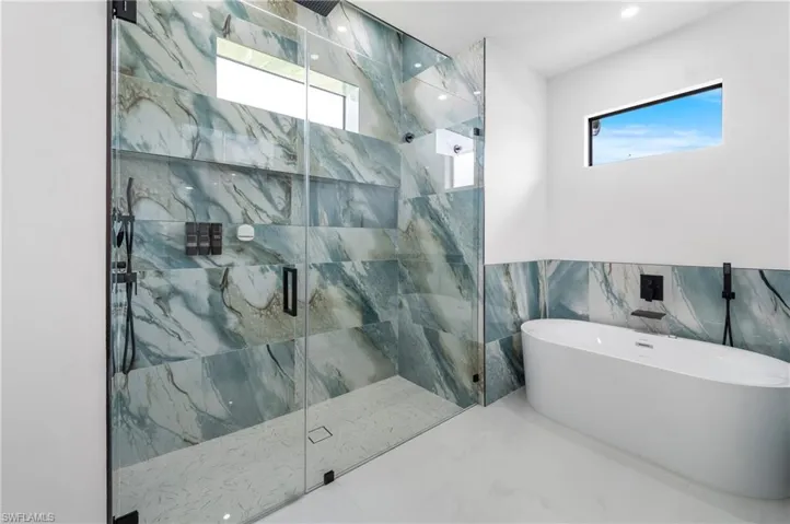 Spacious bathroom featuring a frameless glass shower enclosure, a freestanding oval soaking tub, and large format wall tiling with a natural stone pattern
