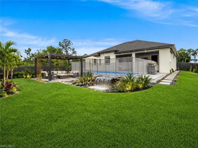 Expansive lawn with a modern pergola-covered patio, a swimming pool with a safety fence, and a decorative waterfall feature