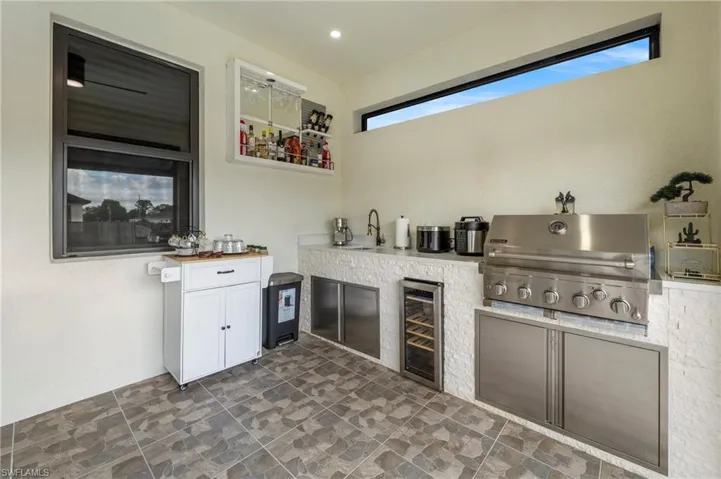 Outdoor kitchen featuring a built-in stainless steel grill, integrated wine refrigerator, and a sink with a wall-mounted faucet