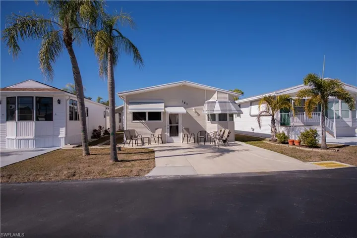 Single-story exterior featuring a concrete driveway, metal window awnings, and palm tree landscaping