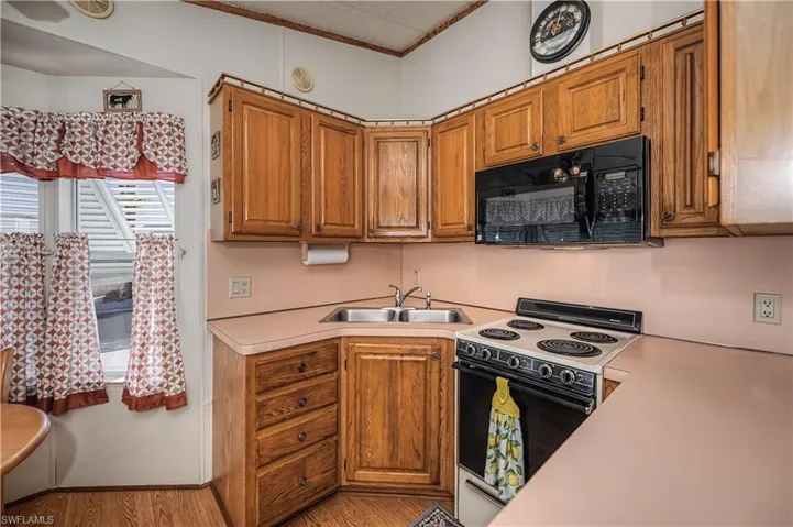 Kitchen featuring wood cabinetry, solid-surface countertops, corner-mounted stainless steel double-basin sink, integrated microwave, and electric range