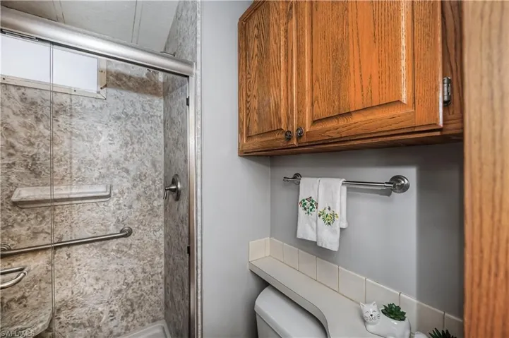 Shower enclosure with textured wall surrounds, built-in soap niche, and metal safety grab bars, complemented by wood-finish wall cabinetry and a tiled vanity backsplash
