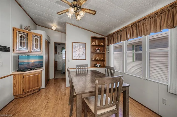Vaulted ceiling featuring a ceiling fan with integrated lighting, wood-finish flooring, built-in wooden cabinetry with glass-panel doors, and built-in shelving