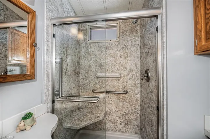 Walk-in shower enclosure featuring floor-to-ceiling patterned surround, integrated corner seat, brushed metal fixtures, and a glass door