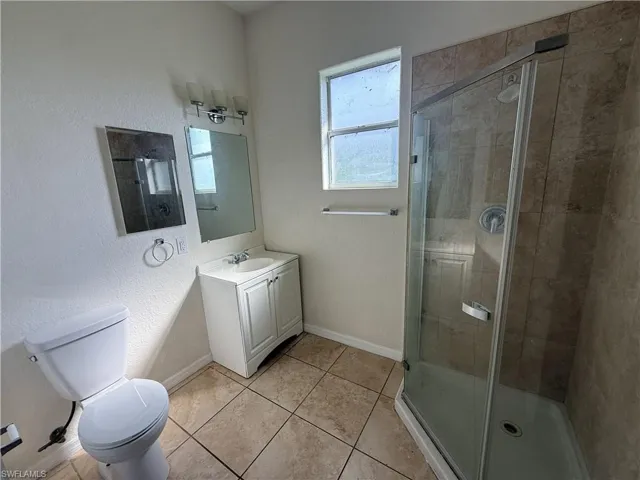 Corner shower with glass enclosure, tile surround, white vanity, and tile flooring