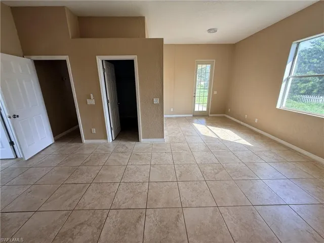 Interior room featuring large-format neutral tile flooring, high ceilings, multiple doorways with six-panel doors, and a full-lite glass-paneled exterior door