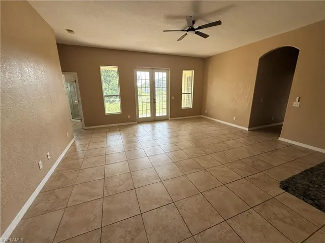 Open-concept space featuring large-format ceramic tile flooring, a centered ceiling fan, double glass-paneled exterior doors, and an arched entry
