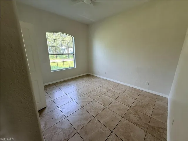 Room featuring large-format stone-finish floor tiling, an arched window with grid mullions, and a ceiling-mounted fan