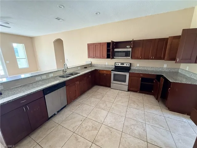 Kitchen featuring stained wood cabinetry, stone-surface countertops, stainless steel appliances, tile flooring, and recessed lighting