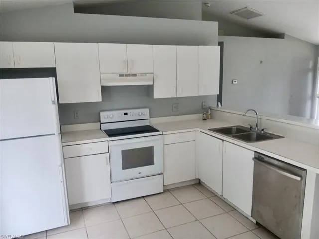 Kitchen with white appliances, light countertops, light tile patterned flooring, and vaulted ceiling